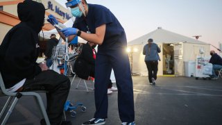 APPLE VALLEY, CALIFORNIA – DECEMBER 18: A California National Guard medic checks vital signs of an incoming patient in front of triage tents set up outside St Mary Medical Center amid a surge in COVID-19 patients in Southern California on December 18, 2020 in Apple Valley, California. The 213 bed capacity hospital in San Bernardino County currently has 60 ICU-level patients with only 20 official ICU beds. The hospital is currently treating 131 COVID-19 positive patients while 20 more patients are suspected to have the virus. Southern California currently has zero percent of its ICU (Intensive Care Unit) bed capacity remaining amid the spike in coronavirus cases and hospitalizations. (Photo by Mario Tama/Getty Images)