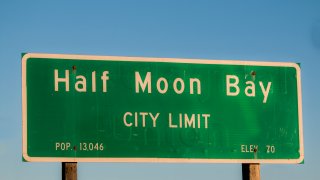 City limits sign for Half Moon Bay California. Standard green sign on wood posts against a blue background.