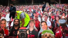 workers install life-sized cutouts of fans in a stadium