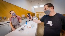 two men in masks converse across a counter