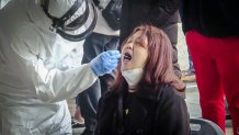 a person in full hazmat gear swabs the mouth of a seated woman