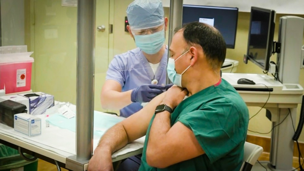 a man in a surgical mask is offered a band-aid after receiving a shot