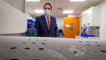 man in a surgical mask opens a freezer with frost lining the inside.