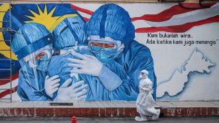 A health worker wearing a personal protective equipment walks past an alley with a mural illustrating medical frontliners outside Clinic Ajwa in Shah Alam, Malaysia.