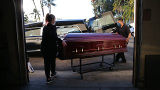Embalmer and funeral director Kristy Oliver and funeral attendant Sam Deras load the casket of a person who died after contracting COVID-19.