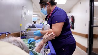 APPLE VALLEY, CALIFORNIA – JANUARY 05: A registered nurse cares for a patient on a stretcher in a hallway of the overloaded Emergency Room at Providence St. Mary Medical Center amid a surge in COVID-19 patients in Southern California on January 5, 2021 in Apple Valley, California. California has issued a new directive ordering hospitals with space to accept patients from other hospitals which have run out of ICU beds due to the coronavirus pandemic. The order could result in patients being shipped from Southern California to Northern California. (Photo by Mario Tama/Getty Images)