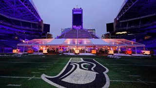 People eat dinner in an outdoor dining tent set up near the logo of the Seattle Seahawks NFL football team