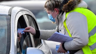 A worker hands-out vaccination cards as members of the public receive vaccinations at a drive-through vaccine center in Hyde, near Manchester, U.K., on Friday, Jan. 8, 2021.