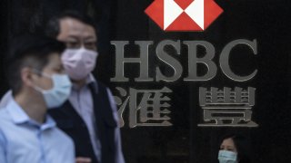 Pedestrians wearing protective masks walk past a logo displayed at a HSBC bank branch in the central district of Hong Kong.