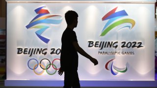 In this 2018 file photo, a visitor walks past logos of the upcoming Beijing 2022 Winter Olympic and Paralympic Games during the Beijing Olympic Expo marking the 10th anniversary of the 2008 Olympic Games, in Beijing.