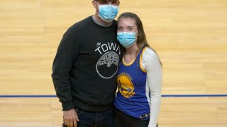 Shelby Delaney, right, an intensive care unit nurse at Oakland's Alta Bates Summit Medical Center, and her husband, Robert Crowley, pose for a photo before the Golden State Warriors and Sacramento Kings NBA basketball game on Sunday, April 25, 2021, in San Francisco. Last spring, Stephen Curry placed a FaceTime call to Delaney and her colleagues at Oakland's Alta Bates Summit Medical Center after learning she was wearing his No. 30 jersey under her scrubs as inspiration to get through each trying day of the pandemic. Delaney wore the uniform again as she and Crowley sat on the floor for Sunday's game after a season ticket holder who couldn't attend gifted her the seats. Inside the jersey reads, "I Can Do All Things."