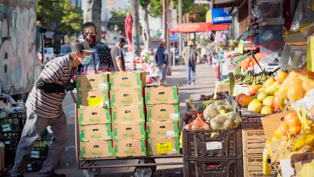 A man pushes a cart full of boxes into the front entrance of a grocery store