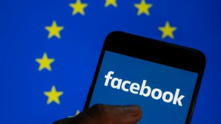 In this photo illustration, the Facebook logo is seen on a smartphone screen with the EU flag in the background.