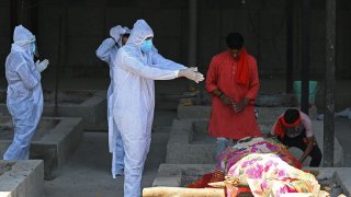 A family member wearing protective gear performs final rites on the funeral pyre of a Covid-19 coronavirus victim at a crematorium in New Delhi on May 24, 2021, as India passed more than 300,000 deaths from coronavirus pandemic.