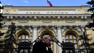 A man on the phone walks past the Russian Central Bank headquarters as the Russian flag flies, in downtown Moscow, on March 19, 2021.