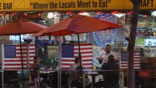 Patrons sits outdoors for dinner separated by plastic dividers with national flags at Mel's drive-in restaurant on Sunset Boulevard on Tuesday, Nov. 24, 2020, West Hollywood, Calif.