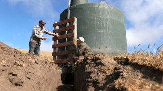 Ranchers Jim Jensen (R) and Bill Jensen (L) stand by a water tank as they work on a water project to try and get more water to their ranch from a well.