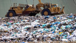 Workers use heavy machinery to move trash and waste at the Frank R. Bowerman landfill on Irvine, California, June 15, 2021.