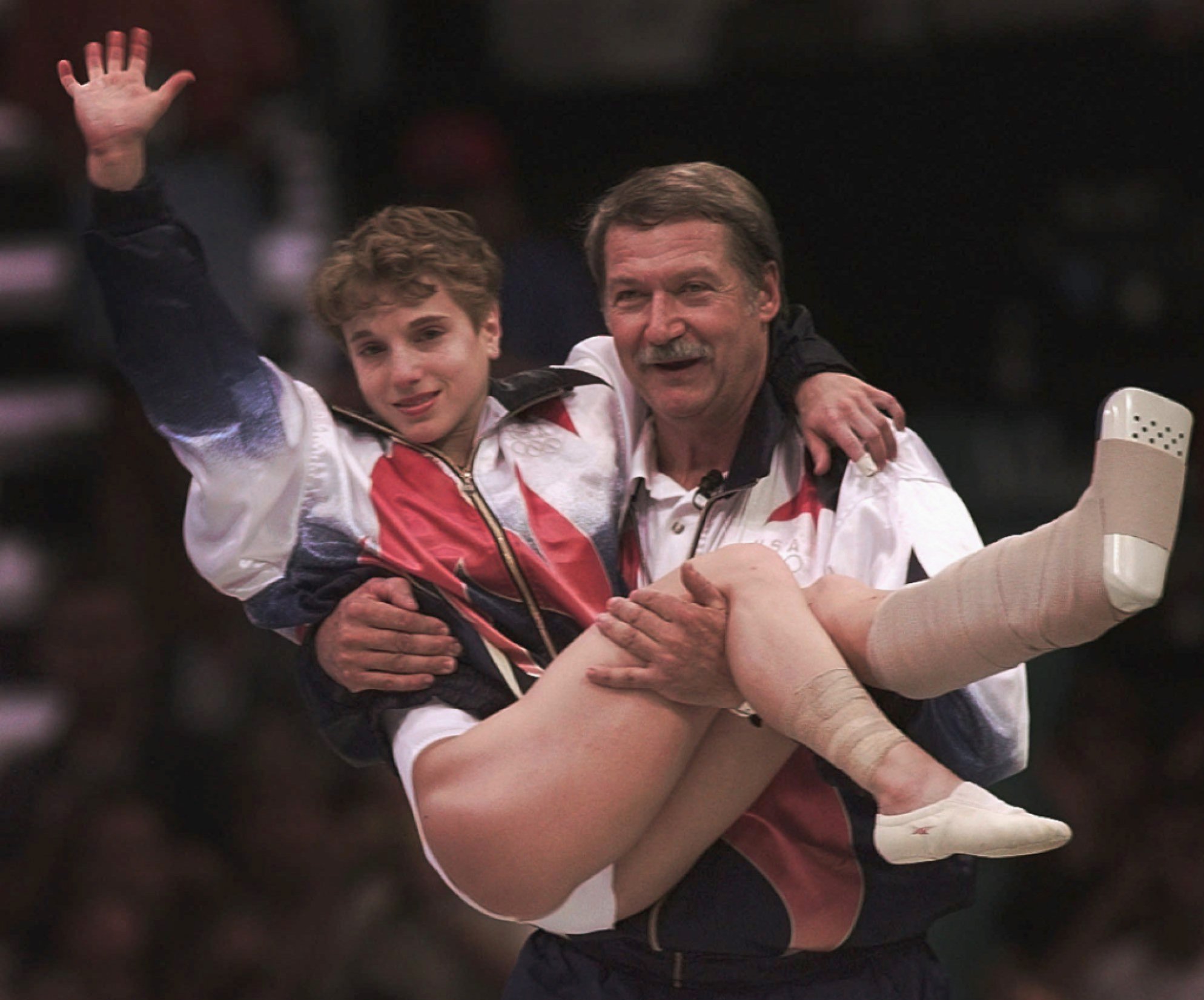 USA's Kerri Strug is carried by her coach, Bela Karolyi, as she waves to the crowd on her way to receiving her gold medal for the women's team gymnastics competition, at the Centennial Summer Olympic Games in Atlanta on Tuesday, July 23, 1996. Strug suffered two torn ligaments and a sprained ankle from the vault competition.