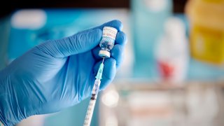 A healthcare Worker hands in surgical gloves pulling COVID-19 vaccine liquid from vial to vaccinate a patient