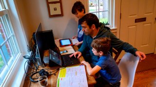 Joachim (R), 8, and Colin (L), 10, whose school was closed following the Coronavirus outbreak, do school exercises at home with their dad