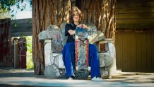 A teenage girl sits with a skateboard on a chair made of skateboards under a tree