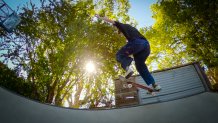skateboarder jumps in the air with trees and a setting sun behind her