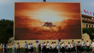 Attendees at a ceremony to mark the 100th anniversary of the founding of the ruling Chinese Communist Party pass by a screen depicting China's Mars spacecraft with its rover landing in Beijing