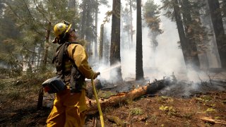 San Jose firefighter Ryan Godoy uses a hose to extinguish hot spots while battling the Dixie Fire on August 12, 2021 near Westwood, California.