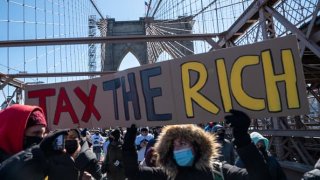 Protestors march across the Brooklyn Bridge holding a sign to “tax the rich” to demand funding for excluded workers in the New York State budget on March 5, 2021 in New York City. crisis.