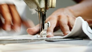 Close-up of Man Worker Sewing Clothing in Garment Factory