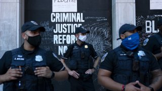 Police officers wearing protective masks stand in front of a criminal justice reform sign