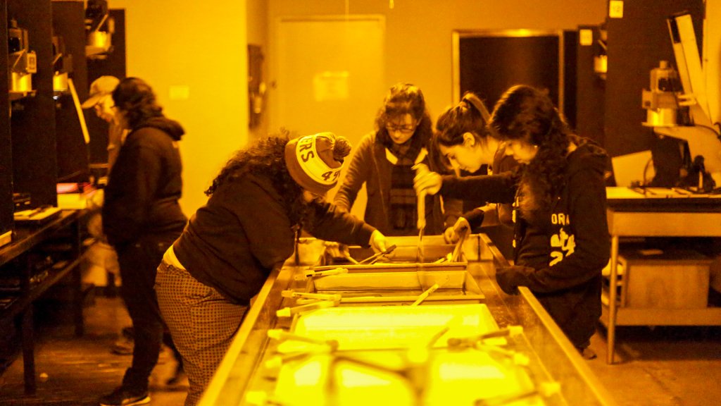 students crowd around a darkroom sink under orange light