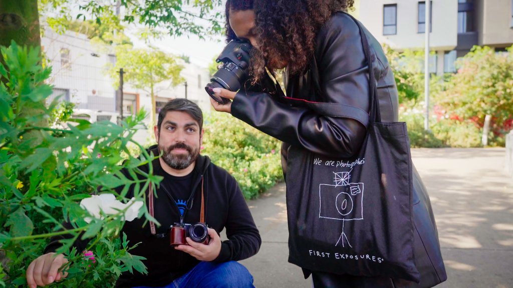 teen girl photographs a flower as a bearded man holds it still for her