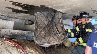 Firefighters remove a mattress and other items from a freeway crawlspace in Sacramento.