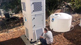 Ted Bowman, design engineer with Tsunami Products, installs a unit in homeowner Don Johnson’s backyard in Benicia, Calif., Sept. 28, 2021. The recent invention can make water out of the air and in parched California, some homeowners are already buying the pricey devices. The air-to-water systems work like air conditioners by using coils to chill air, then collect water drops in a basin.