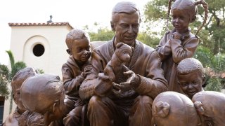 This undated photo provided by Rollins College shows a bronze sculpture of Fred McFeely Rogers, better known as Mister Rogers, at Rollins College, in Winter Park, Fla. Rogers graduated from the central Florida school in 1951. Now he's best known for writing and appearing in 912 episodes of “Mister Rogers’ Neighborhood." The sculpture shows Rogers in his iconic sweater and tennis shoes, surrounded by children.