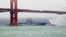 A large Navy ship sails under the Golden Gate Bridge