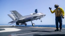 A fighter jet launches from the deck of a Navy ship.