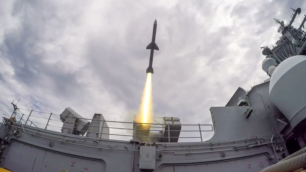 A missile is launched from the central island of a Navy aircraft carrier.