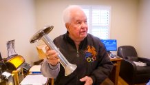 a white-haired man holds a shiny silver object shaped like a mushroom