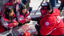 children look at Olympic pins laid out on boards on the sidewalk by a pin trader