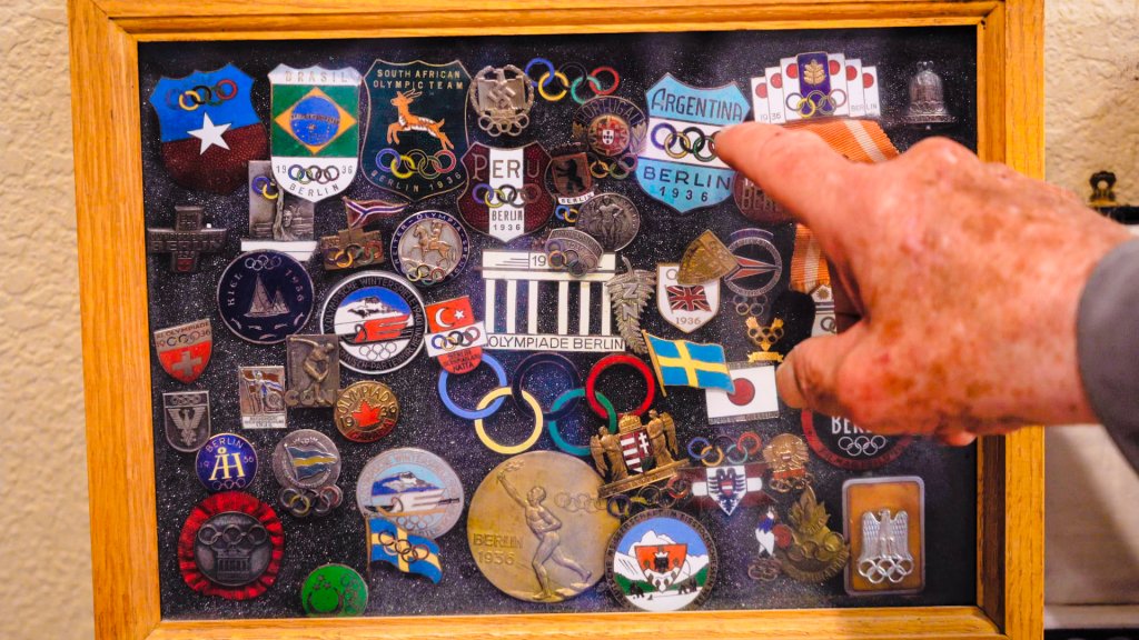 a hand points to a display case of 1936 olympic pins