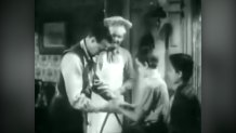 blurry black and white image of two men checking children's hands for cleanliness before a meal. one of the men is wearing a chef's hat.