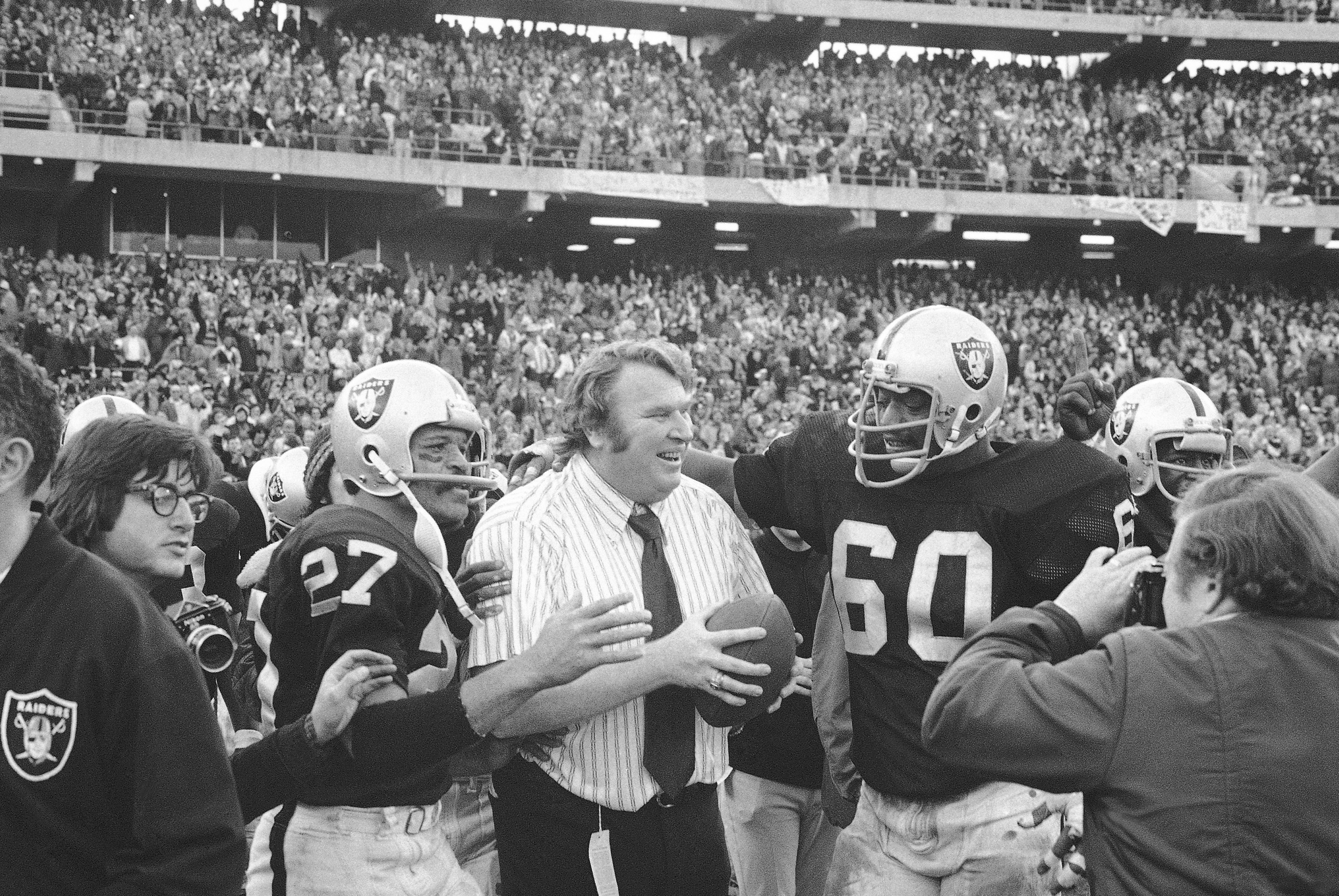 In this Dec. 21, 1974, file photo, Oakland Raiders coach John Madden holds the ball which was used to score the winning touchdown against the Miami Dolphins in an NFL football playoff game in Oakland, Calif. With Madden are Otis Sistrunk (60) and Ron Smith (27). The Raiders won 28-26.