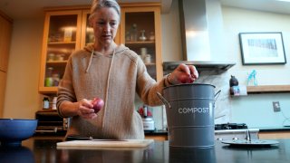 Joy Klineberg tosses an onion peel into container to be used for composting while preparing a family meal at her home in Davis, Calif., Tuesday, Nov. 30, 2021.