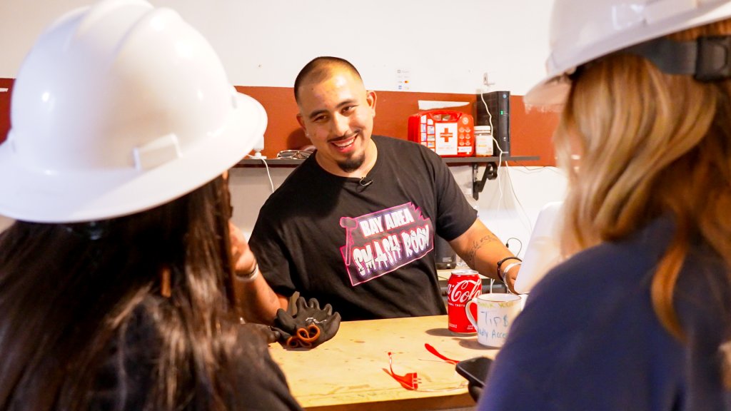 a man smiles at customers wearing hard hats from across a counter