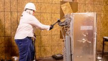 A woman bangs on a half-broken refrigerator with a large hammer