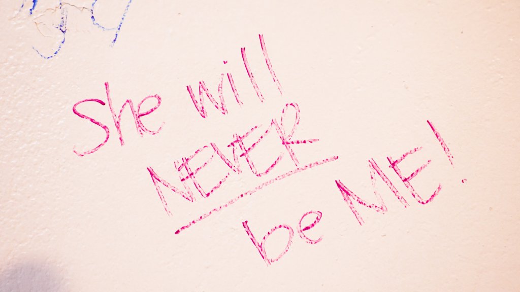 "she will never be me" written in marker on a white wall