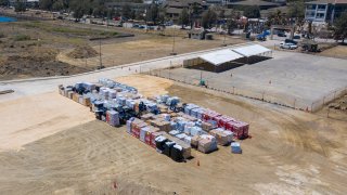 In this photo provided by the Australian Defence Force, aid supplies are stacked at the port at Nuku'alofa, Tonga, Thursday, Jan. 27, 2022, after HMAS Adelaide carried in the disaster relief and humanitarian aid supplies. The danger of spreading the coronavirus was underscored when nearly two dozen sailors aboard the the Adelaide were reported infected on Tuesday, raising fears they could bring the coronavirus to the small Pacific archipelago devastated by an undersea volcanic eruption and a tsunami on Jan. 15.